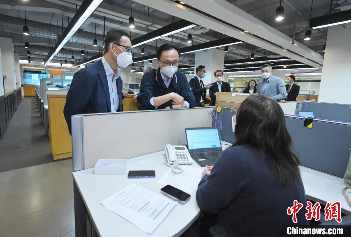 聂德权(左二)与在电话热线中心协助市民登记“疫苗到户接种服务”的明爱专上学院学生交谈。　香港特区政府新闻处供图