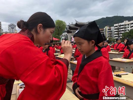 资料图：在“点朱启智”环节，先生在学童的额心点上朱砂，寓意孩子从此开启智慧，目明心亮。晓东 摄