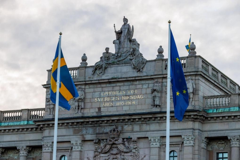 2023年1月1日，在瑞典首都斯德哥尔摩，瑞典议会大楼外悬挂瑞典国旗和欧盟旗帜。（图源：新华社）